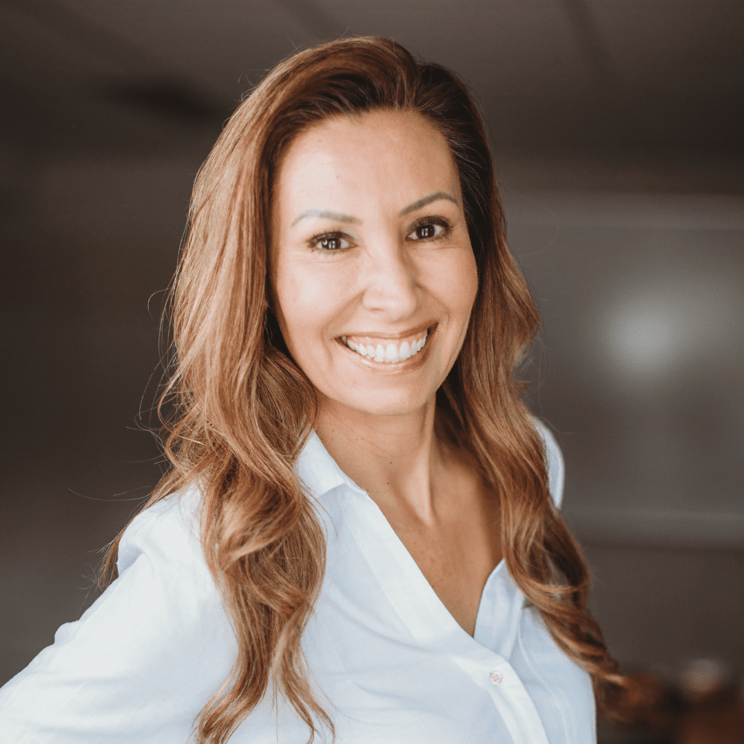 Darla stands smiling in a boardroom wearing a white button-up shirt.